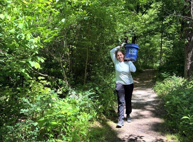 A volunteer carries a bucket on her shoulder on a trail in Mammoth cave national park