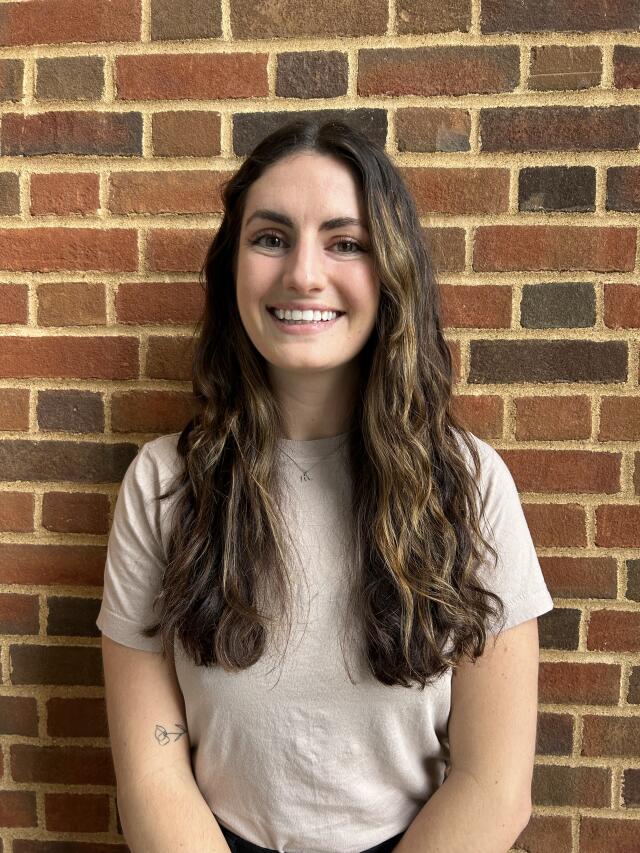 Photo of a white woman with brown curly hair and a tan shirt smiling