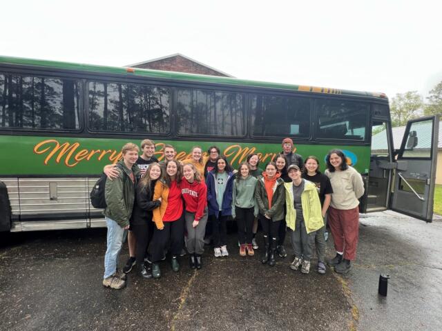 Group of college students posing outside in front of Merry Green Marvel adventure coach bus