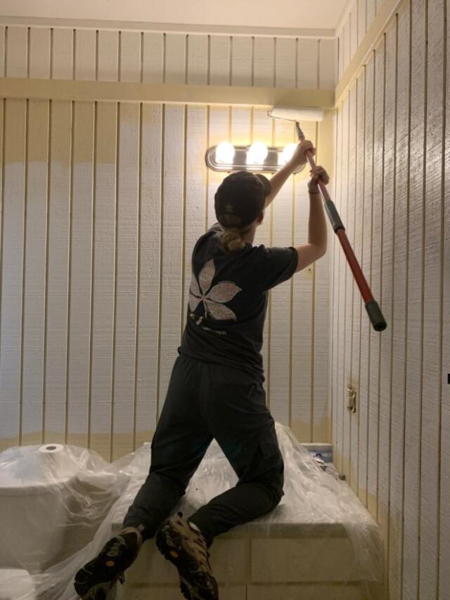 College student volunteer kneeling on top of counter and painting wall