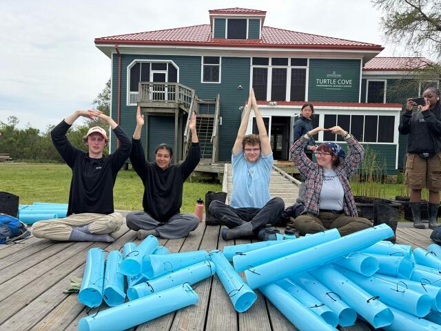 Four students sitting on a deck posing in O-H-I-O while serving with Merry Green Marvel