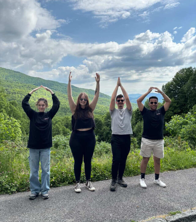 Four students pose for O-H-I-O with rolling hills in the background