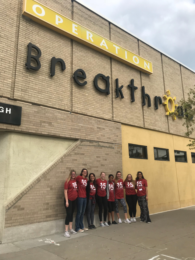 8 college student volunteers wearing red t-shirts in front of Operation Breakthrough building