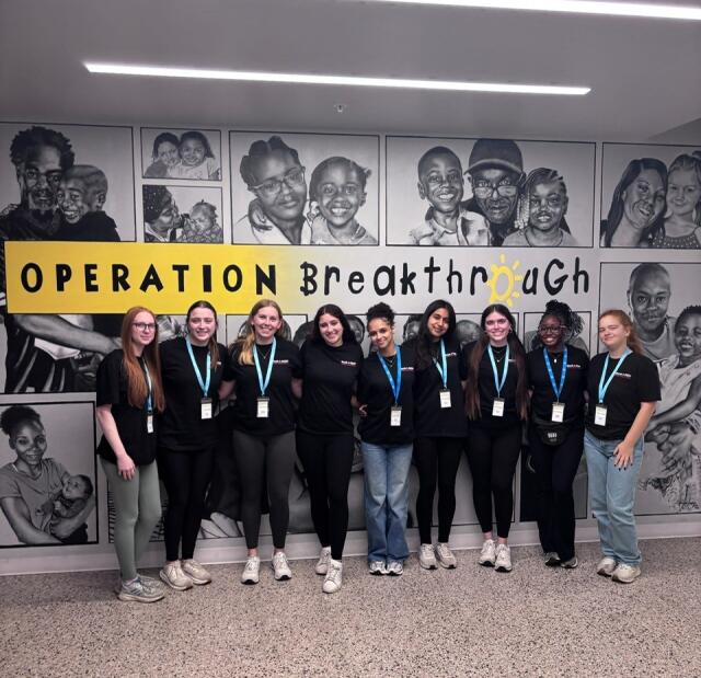 Students pose in front of indoor Operation Breakthrough sign and mural