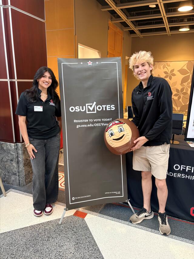 OSU Votes student assistants smiling by a voter registration banner with a Brutus Buckeye ball.