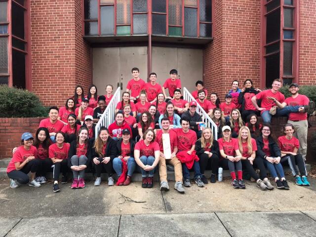 Large group of college student volunteers wearing red t-shirts sit on steps outdoors