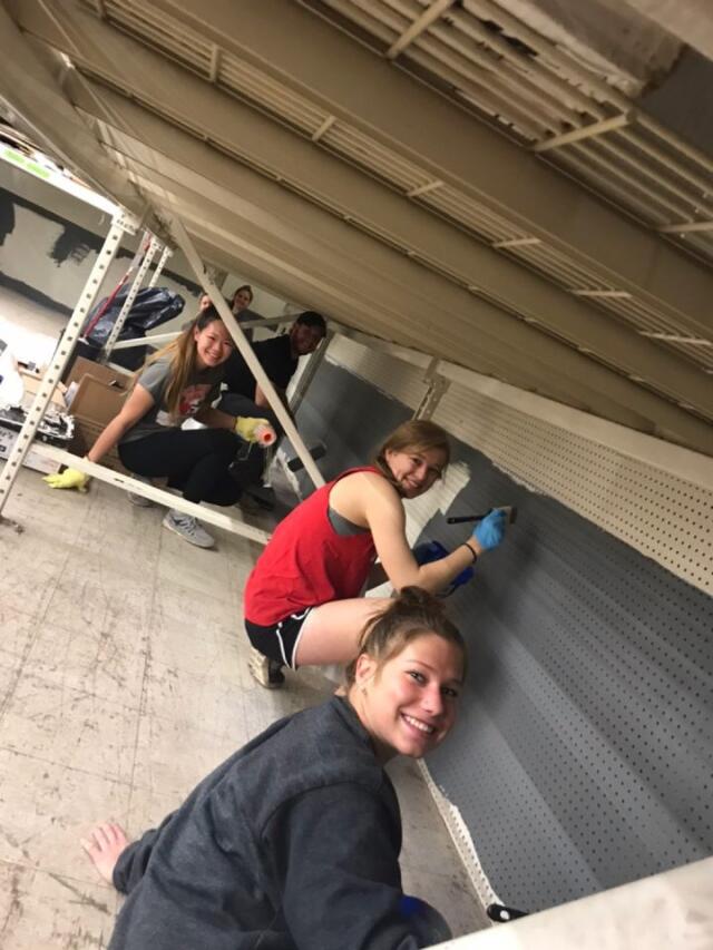 6 college student volunteers painting a side wall dark gray