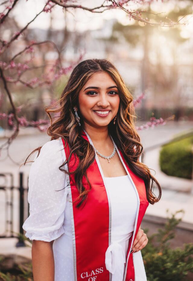 A smiling woman in a white dress wearing a red graduation stole