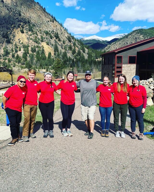 7 student volunteers gathered with Rocky Mountain Village staff member in front of mountains
