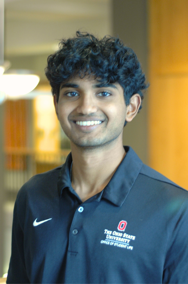 A man in a black polo smiles